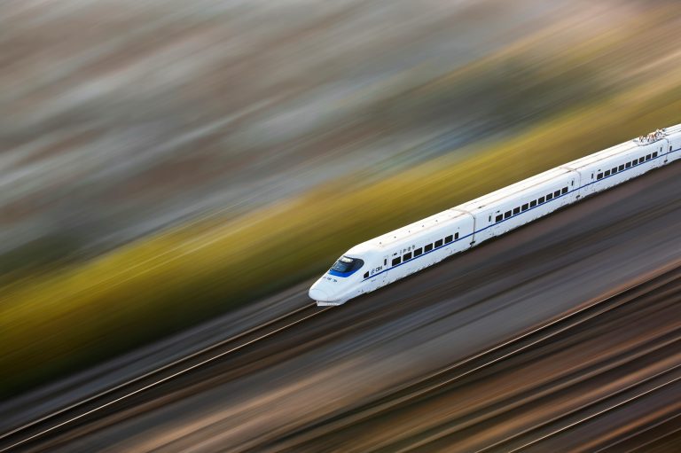 A sleek white high-speed train traveling at top speed, captured with a motion blur effect.