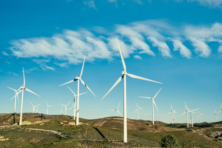 Scenic view of wind turbines on hills under a clear blue sky, symbolizing renewable energy.