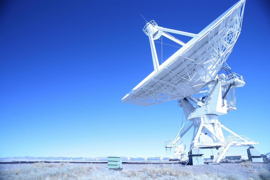 A large satellite dish observatory against a clear blue sky in a desert landscape, capturing signals.