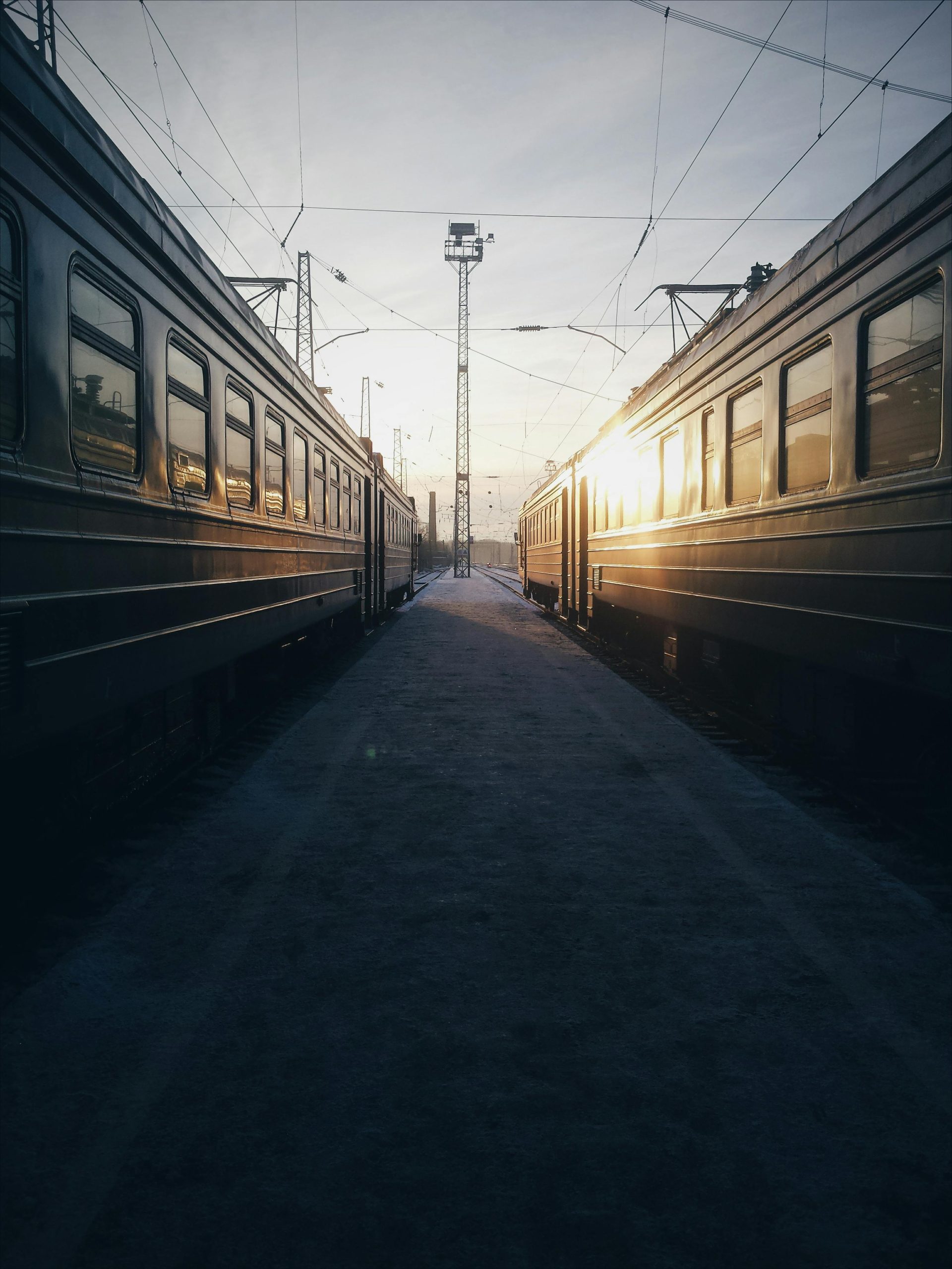 Sunrise between two trains at an empty station, showcasing railway symmetry.