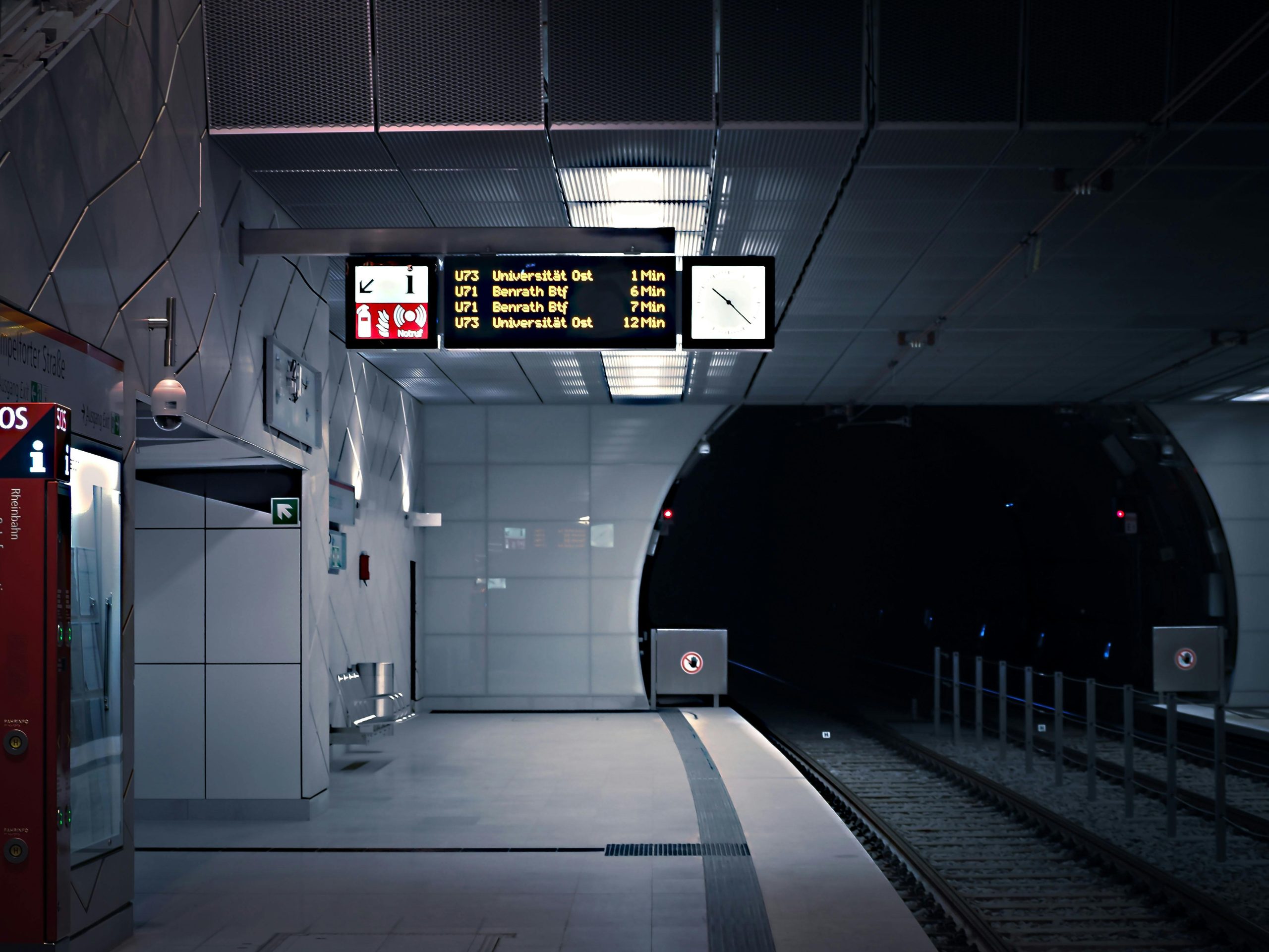 Empty and modern subway platform with illuminated signs and tracks leading into a tunnel.