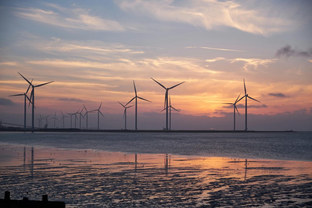 Wind turbines on the shoreline silhouette against a vibrant sunset, promoting renewable energy.