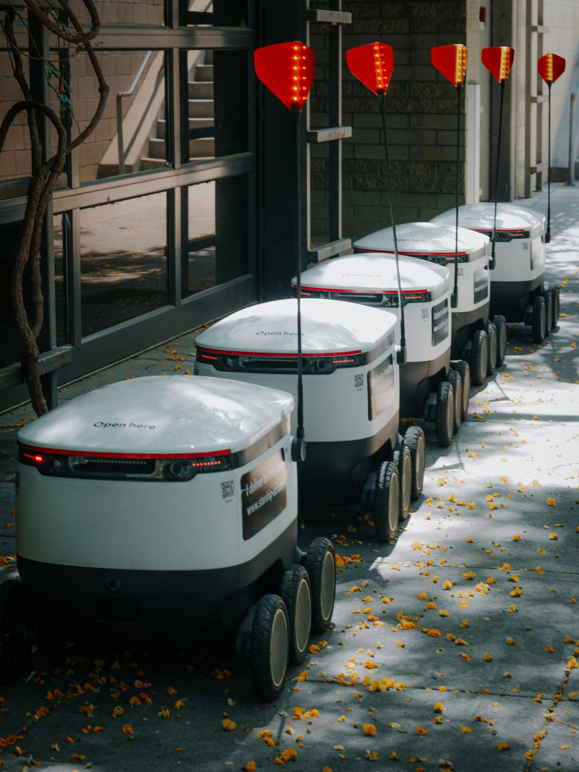 Line of autonomous food delivery robots on urban path under trees.