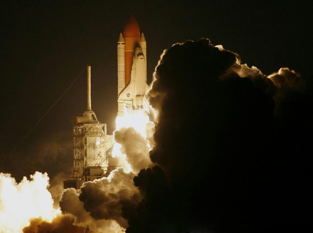 Dramatic capture of a space shuttle launching into the night sky, shrouded in smoke.