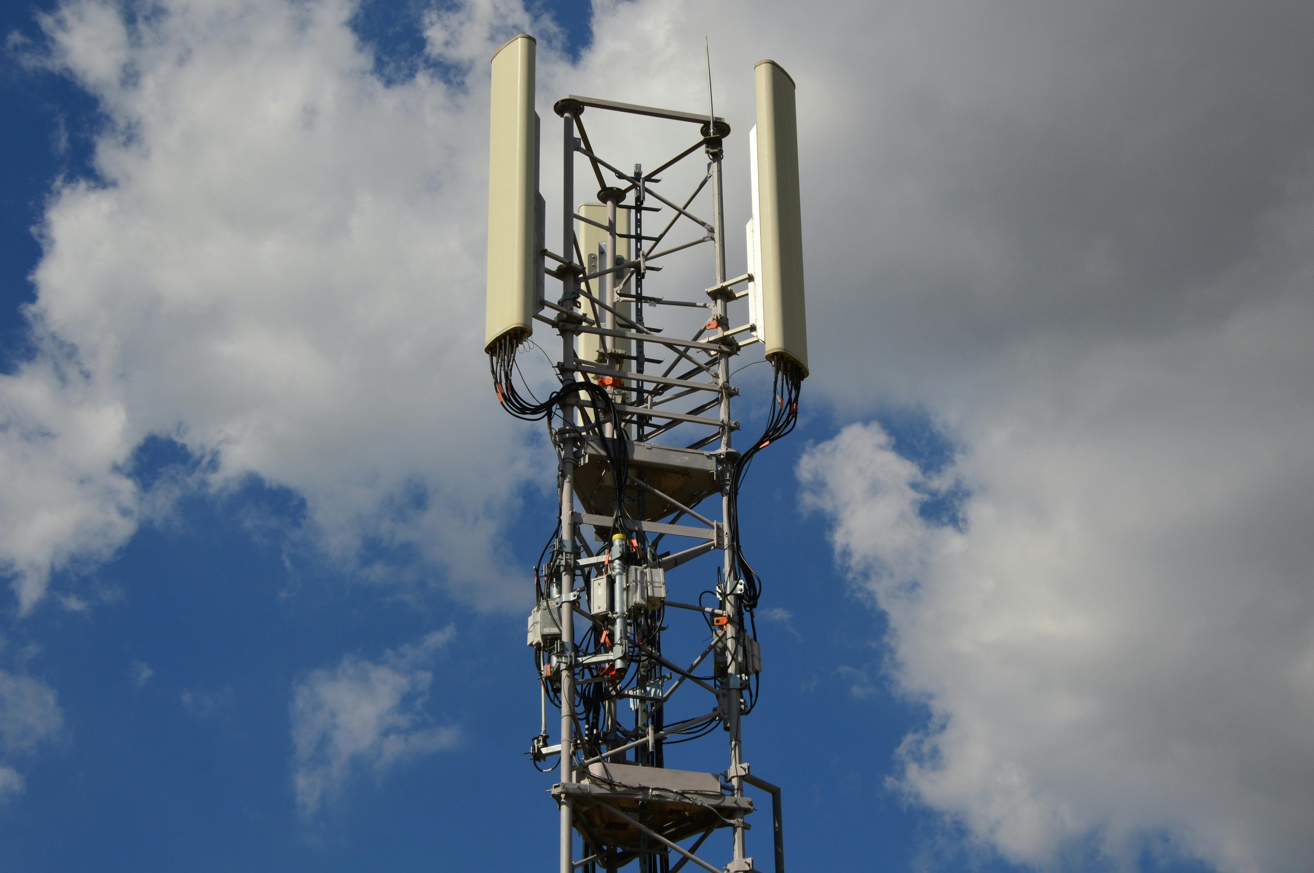 High-angle view of a modern cell tower with technology components against a blue sky with clouds.